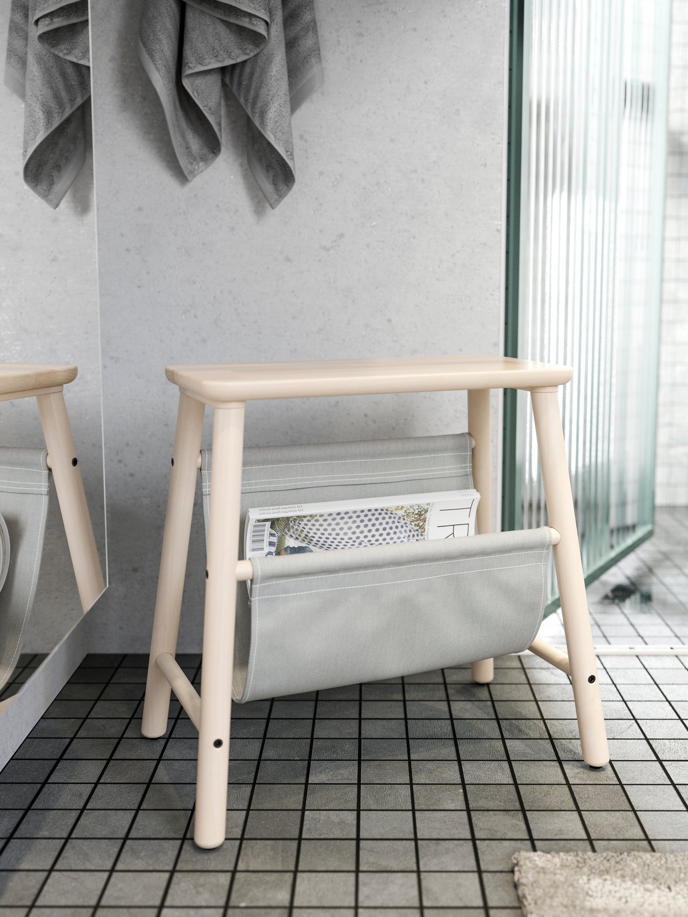 A VILTO storage stool in birch with a pocket containing a magazine, on a tiled bathroom floor next to a shower door.