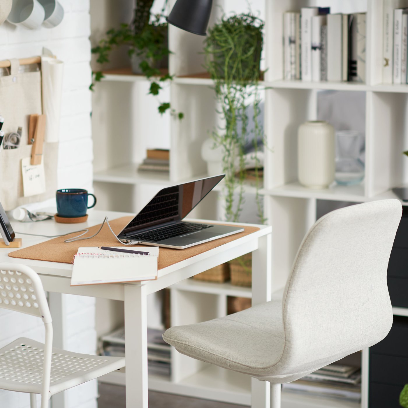 Chaise pivotante blanche devant une table MELLTORP blanche où se trouve un ordinateur portable, près d’une étagère KALLAX blanche.