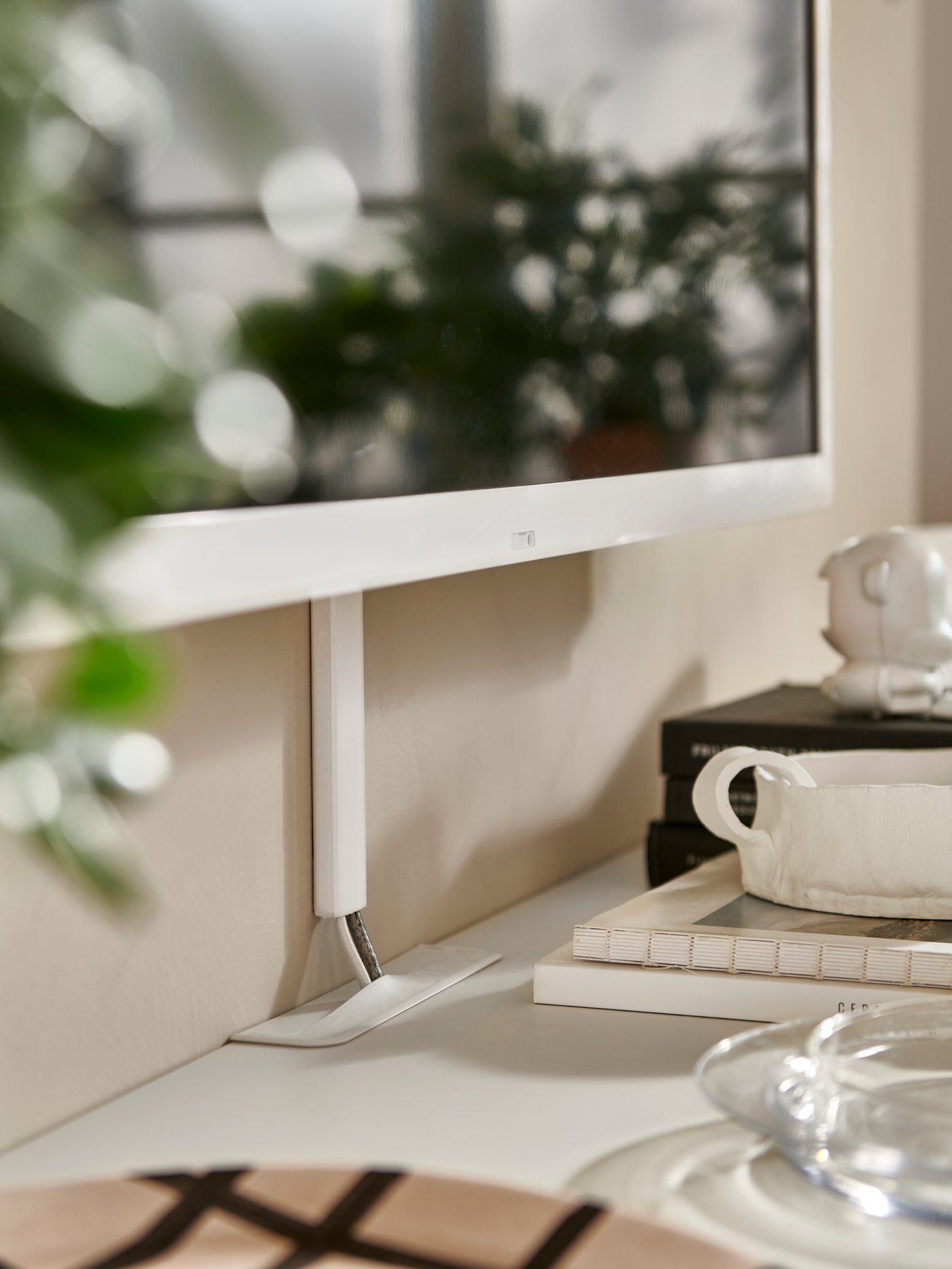 Cables from a wall-mounted TV enter a white BESTÅ TV bench with doors through a cable outlet on the top of the bench.