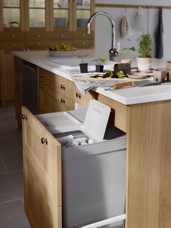 A pull-out door in a kitchen with a white marble effect worktop, holding HÅLLBAR waste bins. One of the bin lids is open.