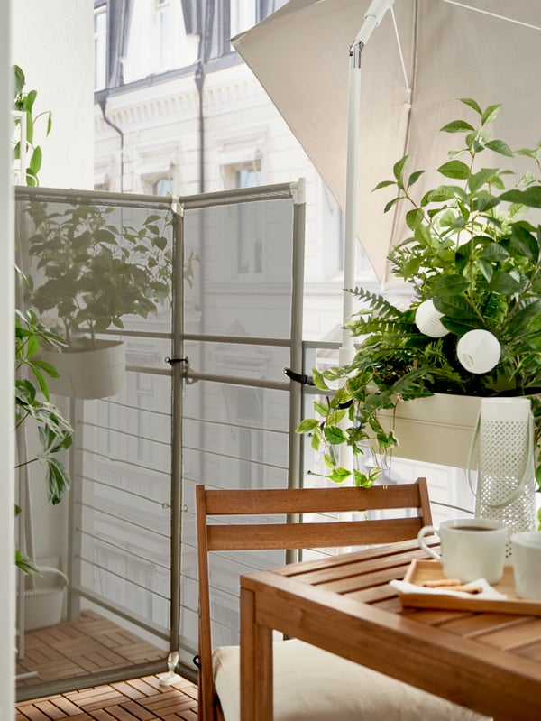 Auf einem Balkon steht ein YTTERSKÄR Sichtschutz und auf der rechten Seite steht ein Tisch mit einer Pflanze darauf.