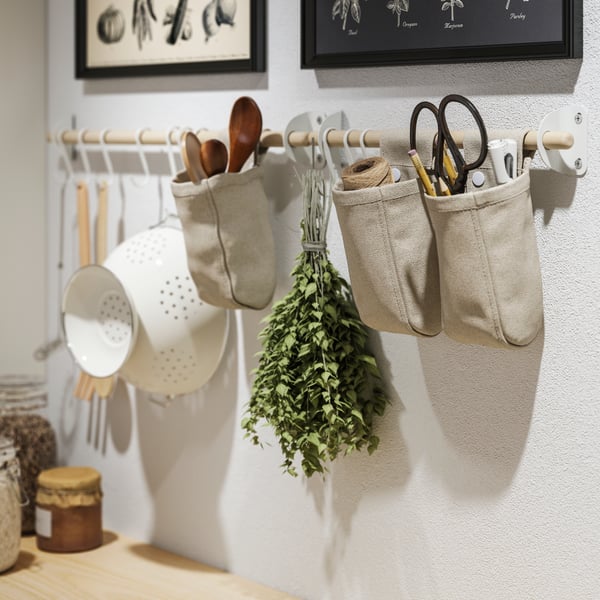 An white colander, cooking utensils and herbs hanging from NEREBY rails on a kitchen wall.