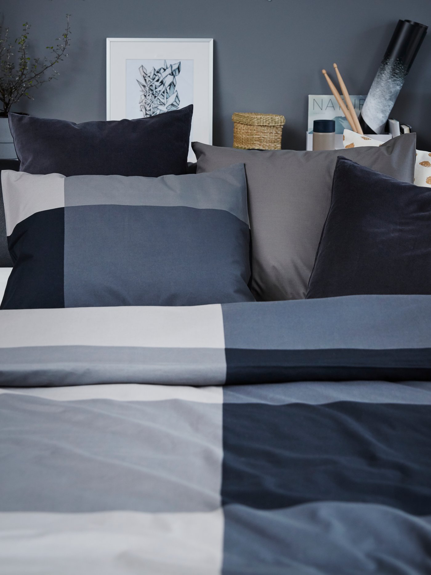 A black leather sofa-bed made up with black/grey bedding and cushions in grey, white/gold and dark cotton.