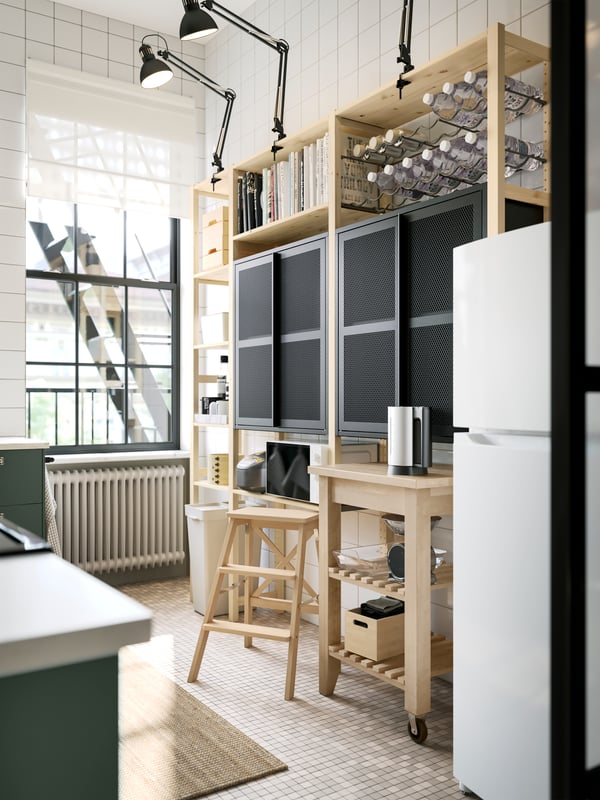 A pine IVAR shelving unit with two black mesh cabinets with doors and dark grey work lamps up top, plus a kitchen trolley.