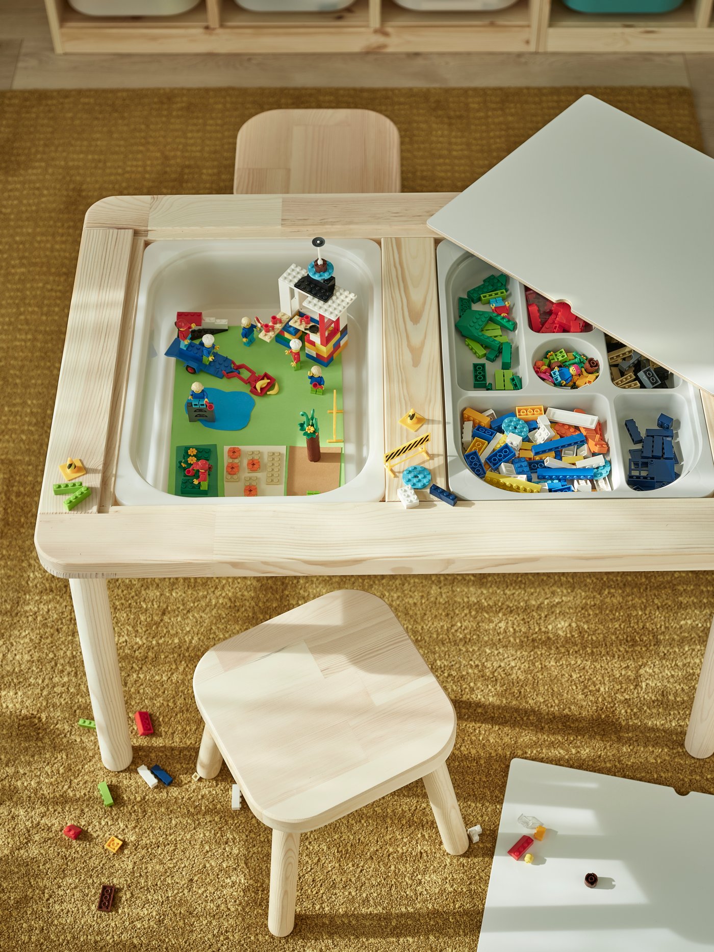 Vista superior de una mesa de madera FLISAT con cajones TROFAST que en su interior tienen juguetes mini.