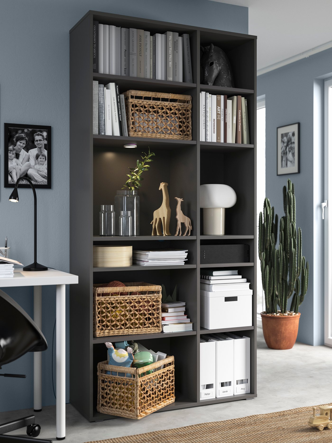 A dark grey VIHALS storage cabinet with 10 shelves, filled with books, figurines, file folders, lighting and other accessories in the living room.