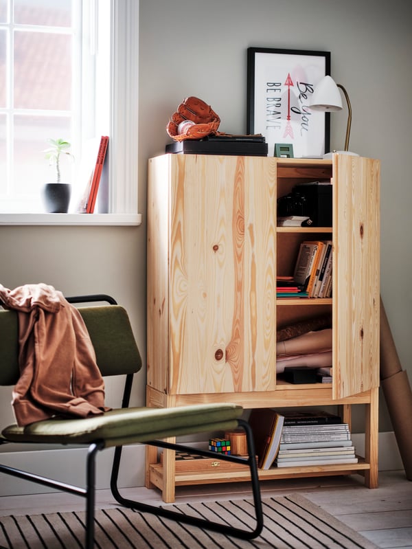 An olive-green LINNEBÄCK easy chair next to a pine IVAR shelving unit with cabinet and an ISNÅLEN LED work lamp on top.