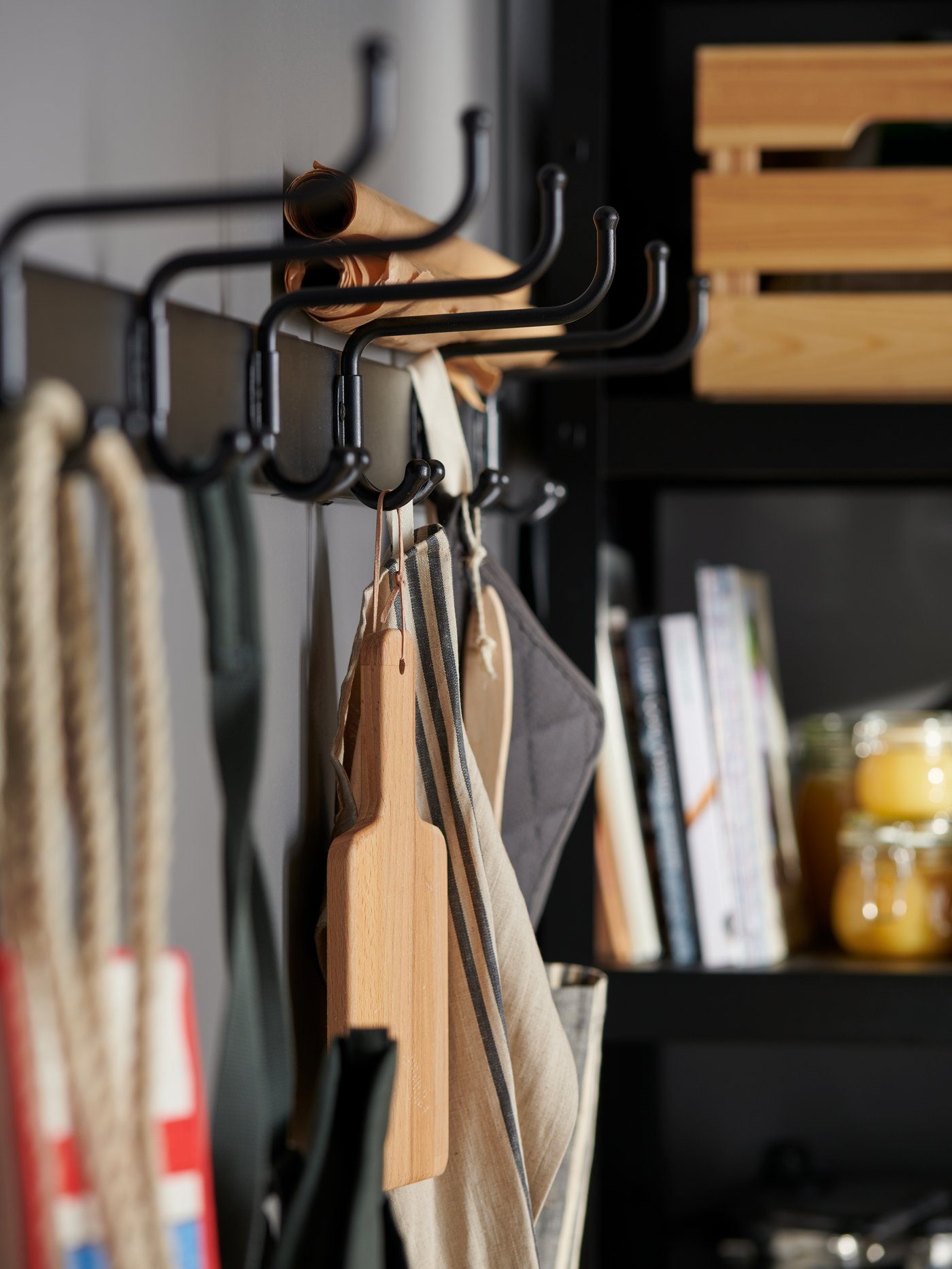 Black PINNIG racks with 3 hooks mounted on a grey wall in the pantry holding wooden kitchen utensil, kitchen towel and bags.