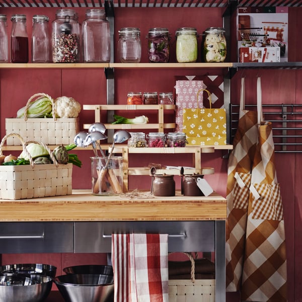 A kitchen with shelves and a table adorned with several KÖSSEBÄR items, like jars, baskets, tea towels, aprons, and more.