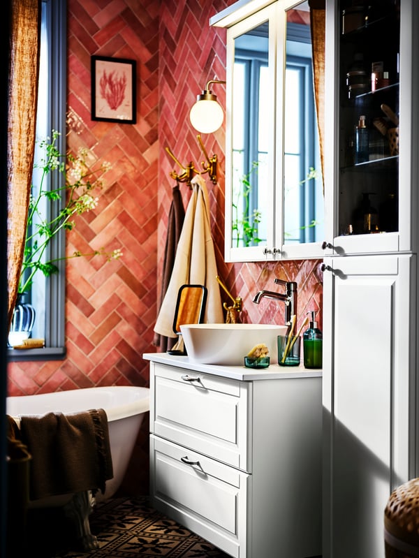 Ecke eines Badezimmers mit rosafarbenen Fliesen, einer Badewanne, einem Waschbeckenschrank, einem Hochschrank und einem Spiegelschrank.