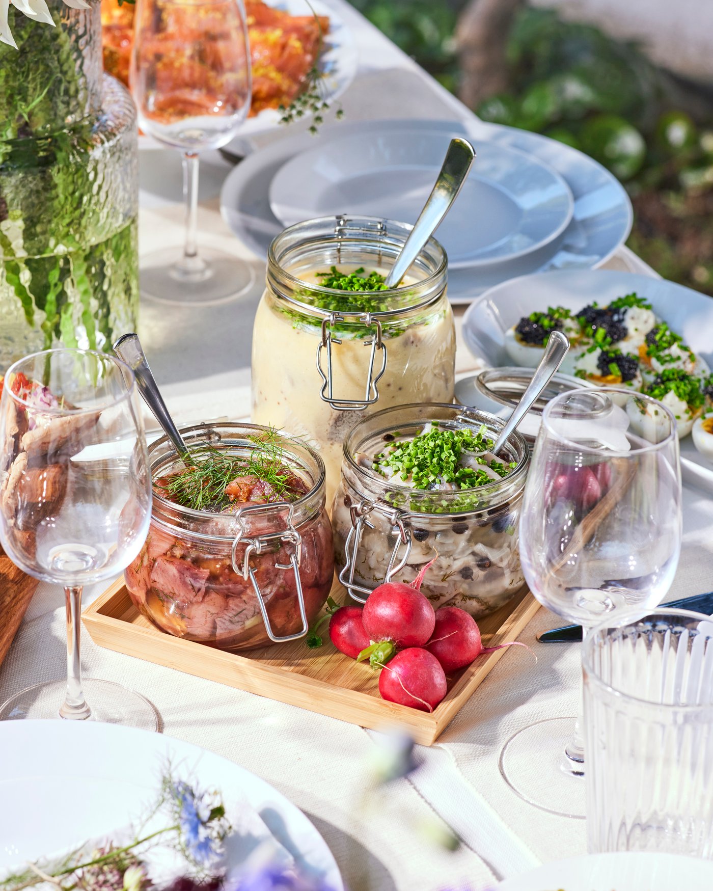 Ett dukat bord med midsommarlunch med sill serverad i glasburkar.