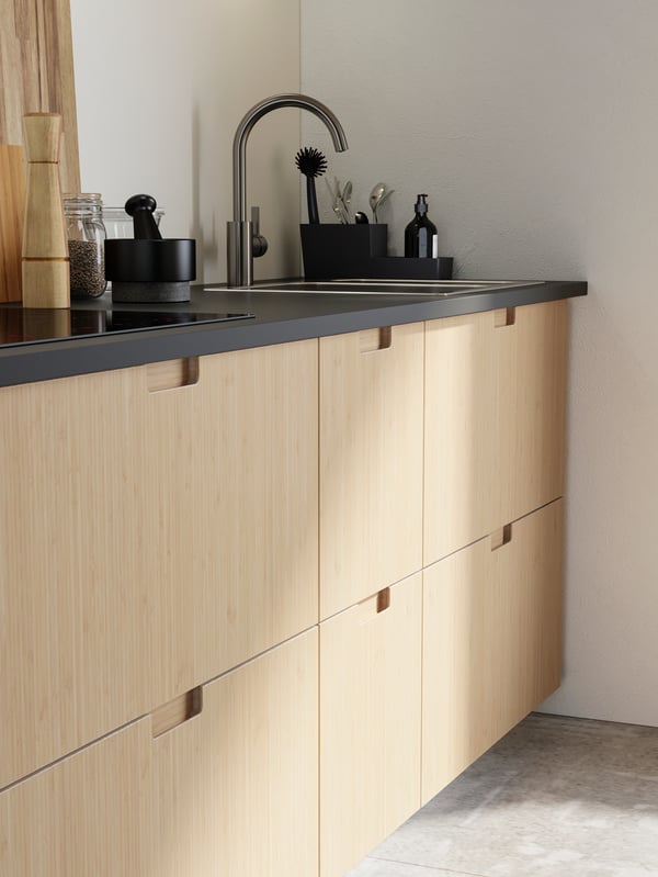 A kitchen with light bamboo drawer fronts, a matte anthracite worktop, a sink with a kitchen mixer tap.