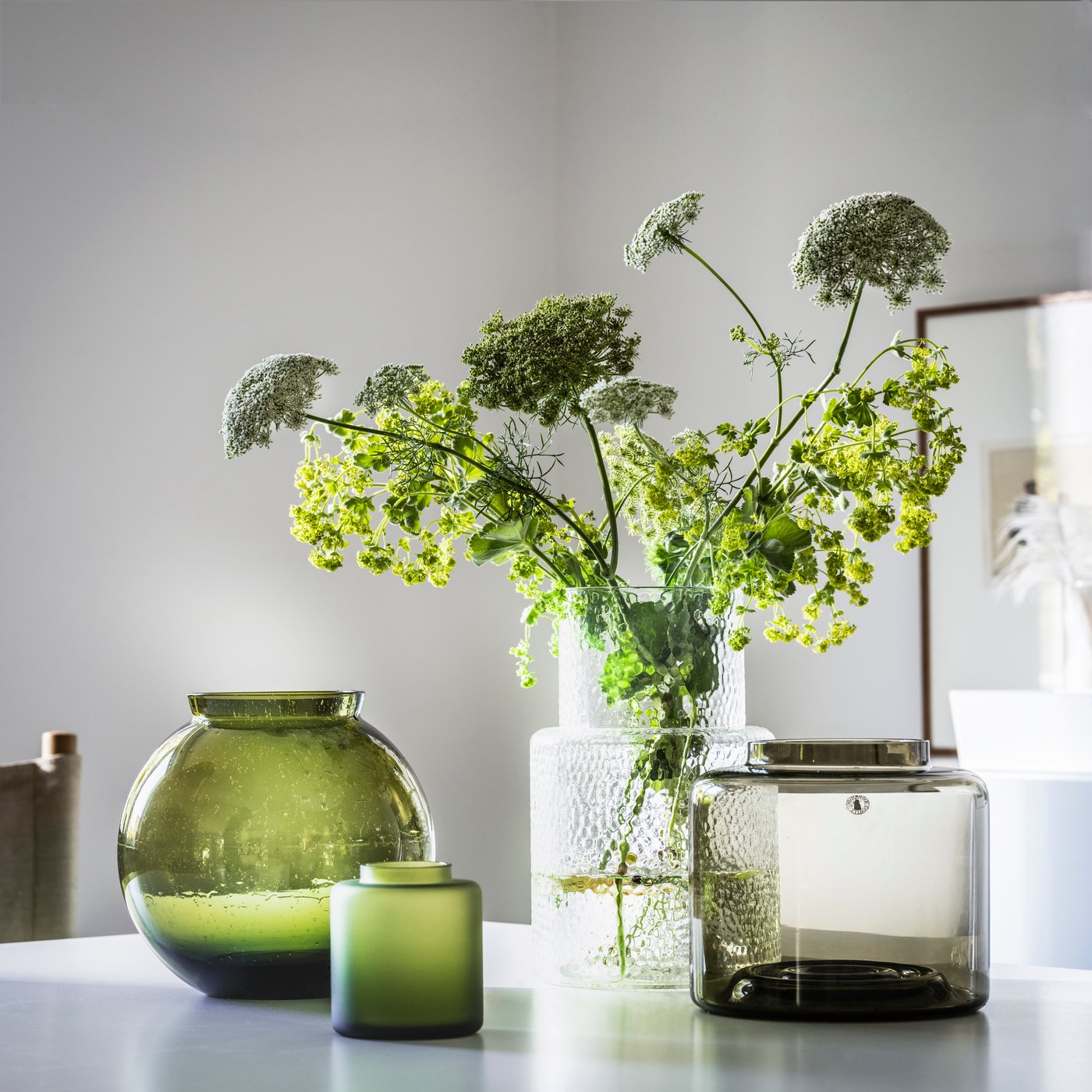 Different types of KONSTFULL vases with flowers in them are placed on a white table in the living room.