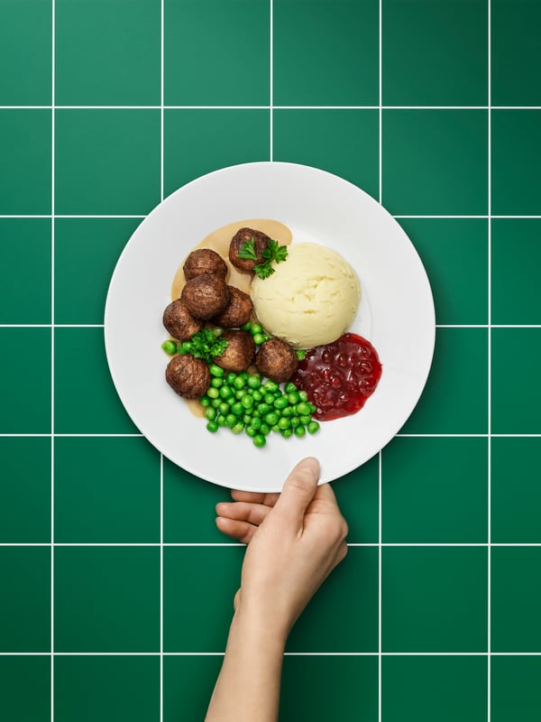 Hand holding a plate of traditional Swedish plant ball serving in front of a green background. 