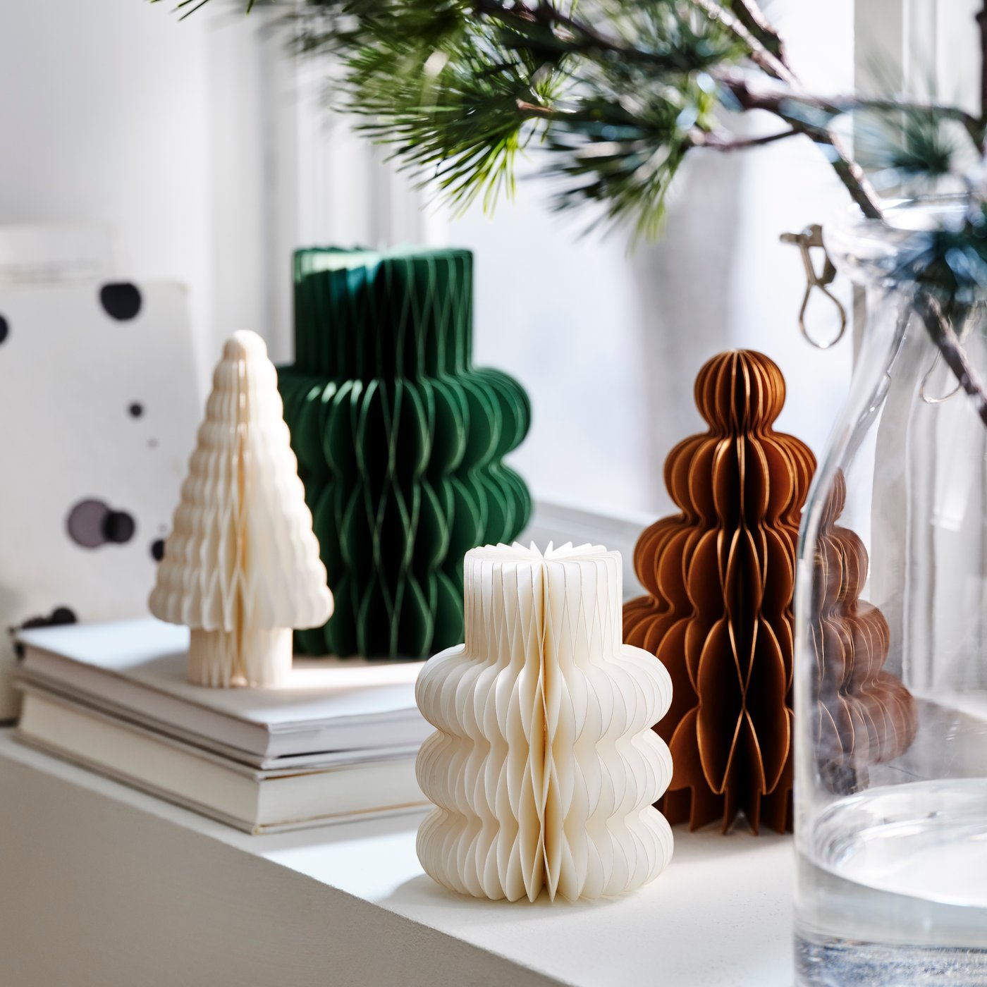 Four paper tree-shaped decorations in a windowsill, two are resting on a stack of two books.