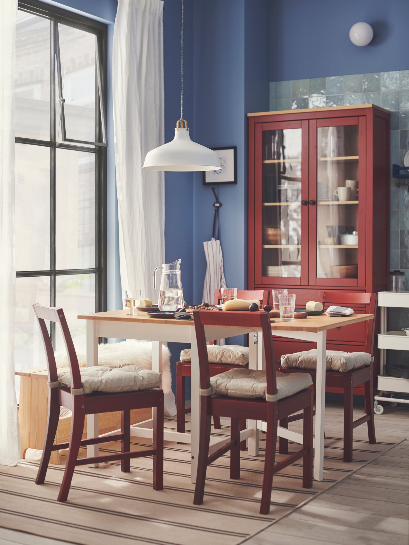 Red glazed PINNTORP chairs and a PINNTORP folding table form the centre of this Swedish country-style dining room. The walls of the room are coloured blue.