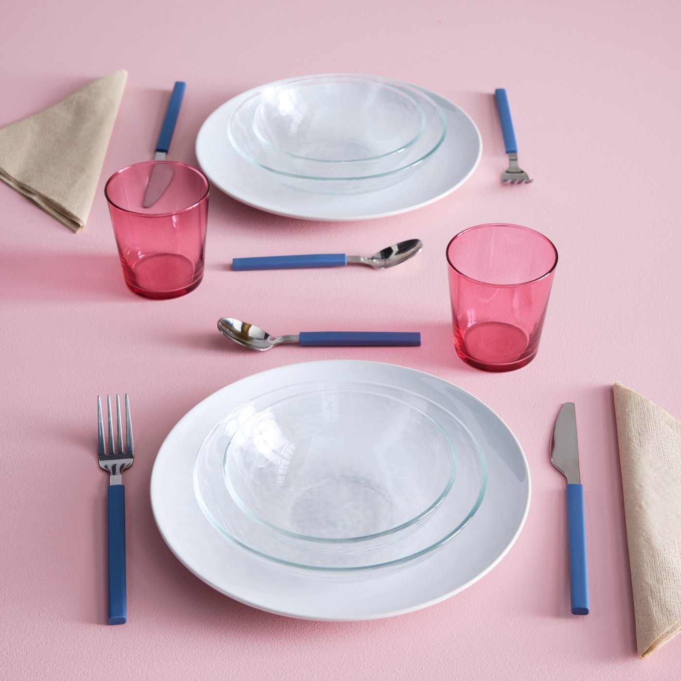 A table setting has white GODMIDDAG plates, clear STRANDKRABBA bowls and pink PAPPERSBJÖRK glasses all on a pink surface.