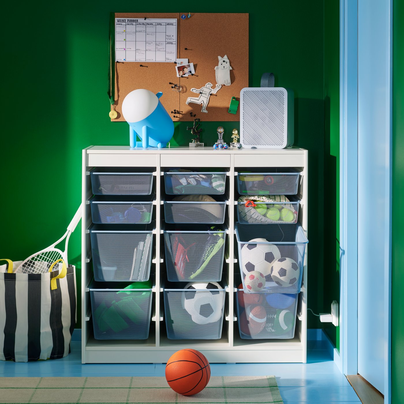A TROFAST combination with mesh storage boxes storing sports balls and equipment, against a green wall in a children’s room.