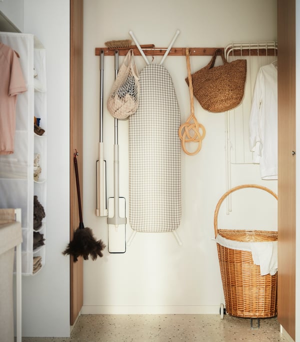 A HÖVOLM coat rack with various cleaning supplies hanging from it in the storage room.