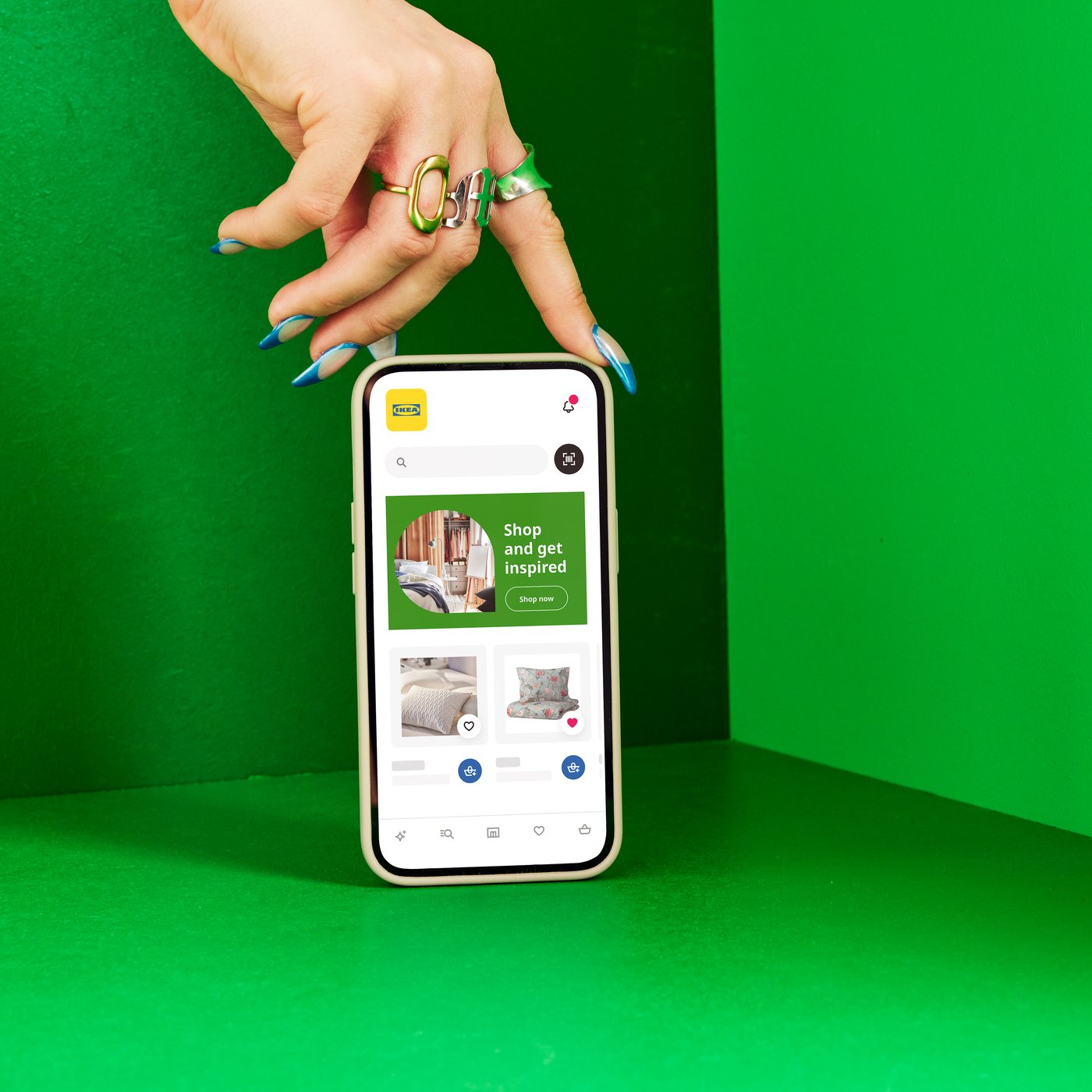Hand with blue nail polish pointing at a smartphone displaying the IKEA app against a bright green background.
