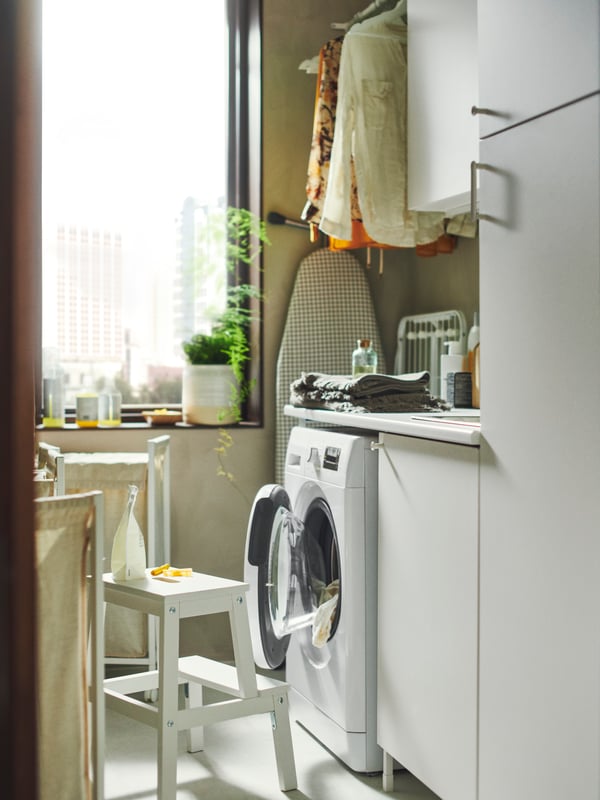 Mueble para lavadero ENHET de estructura blanca con puertas blancas. Junto al mueble hay un piso BEKVÄM blanco. 