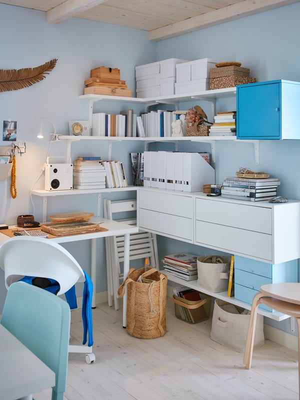 White shelves and wall brackets in the corner of the room with boxes, books, file organisers, a speaker and drawers.