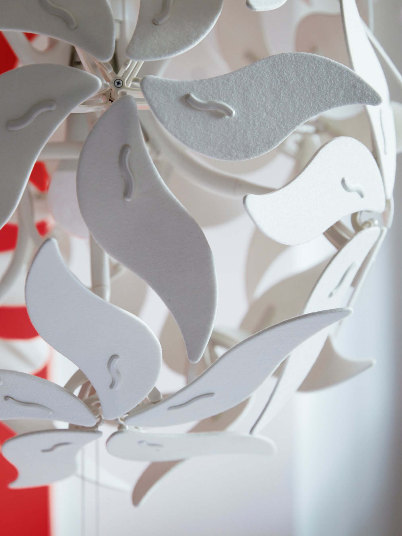 A close up of the flower-shaped RAMSELE pendant lamp in white, with strings, against a red and white background.