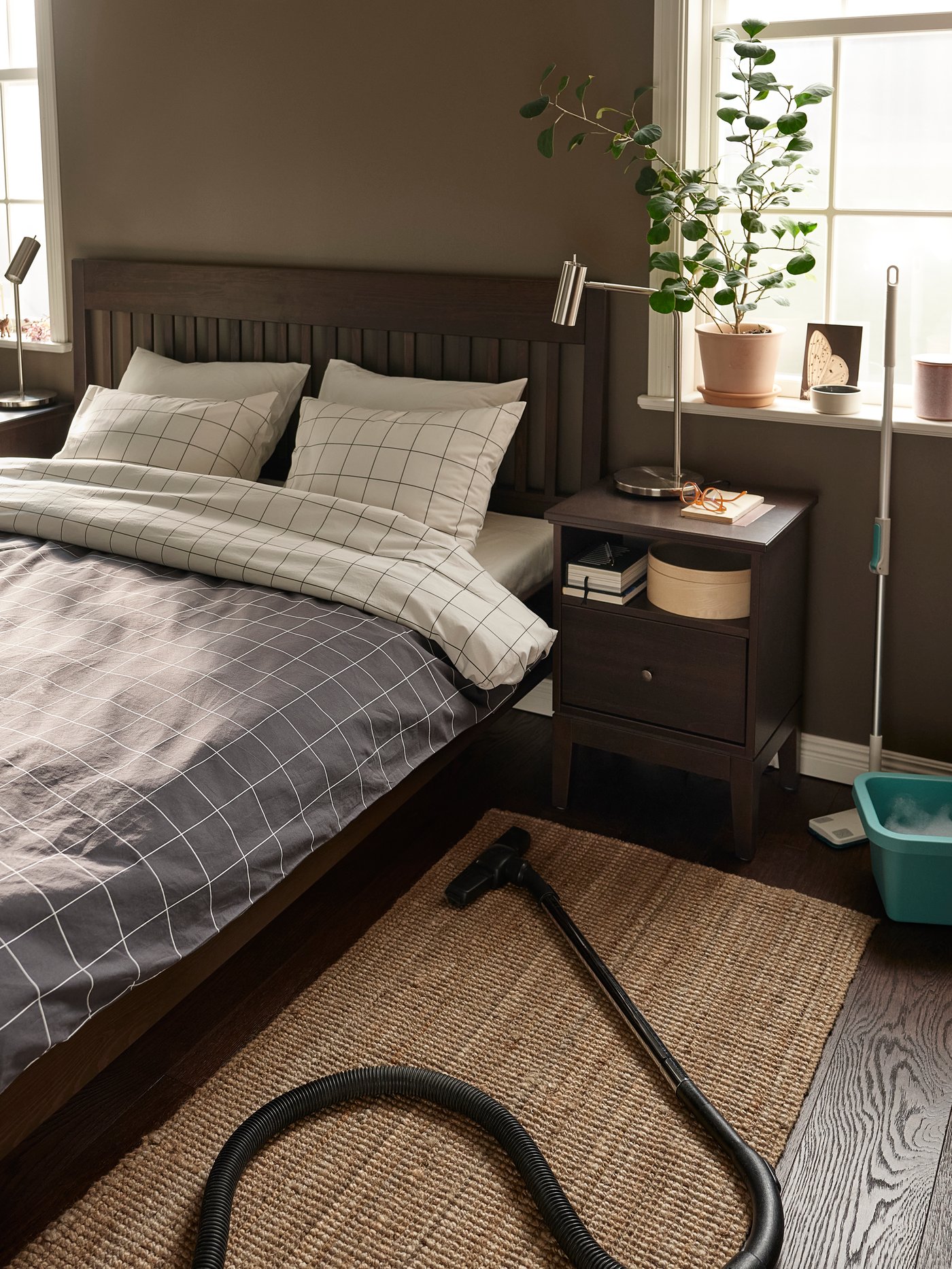En un dormitorio al costado de una cama doble hay una aspiradora sobre un tapete de bajada de cama.