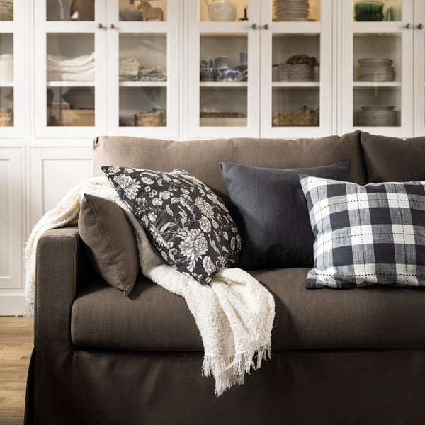 An off-white SANDBRODD throw and some cushions, including one with a floral IDALINNEA cushion cover, lie on a HYLTARP sofa.