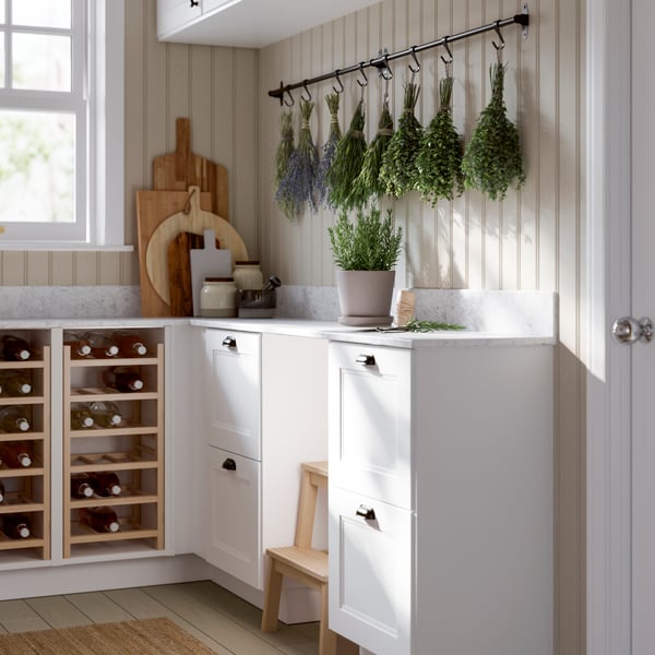 Un garde-manger lumineux présente un range-bouteilles blanc, des fines herbes suspendues et une plante en pot sur le comptoir.