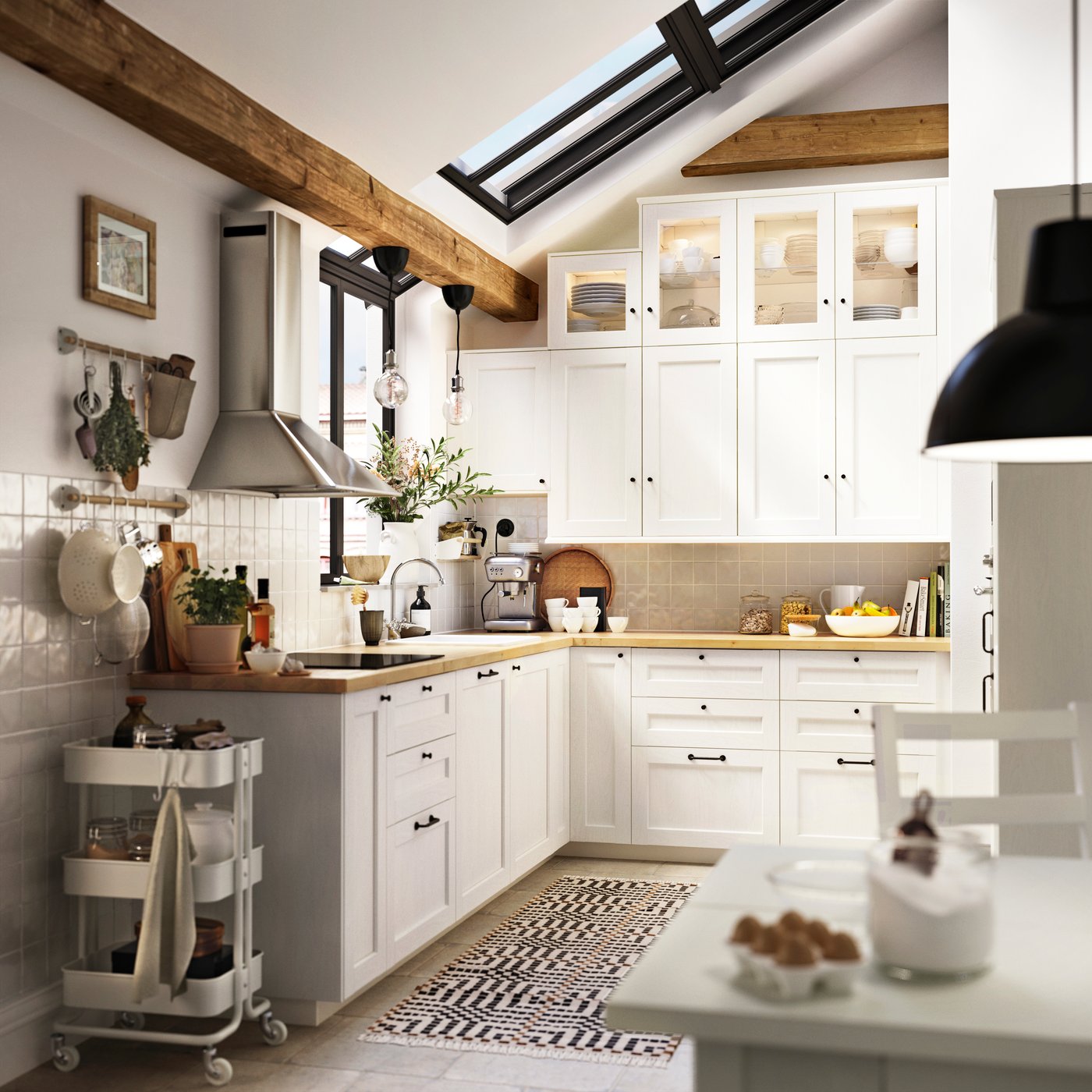 La cocina tiene cajones y armarios colgantes con frentes ENKÖPING blancos y barra HULTARP niquelada con ganchos en la pared.
