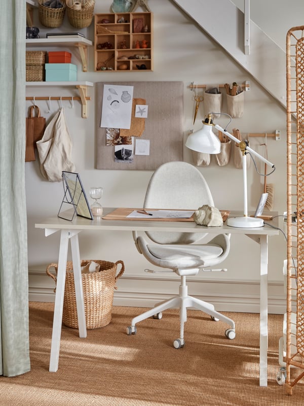 A small workspace beneath a staircase with a TROTTEN desk and a HATTEFJÄLL office chair, amid ample storage and decorations.