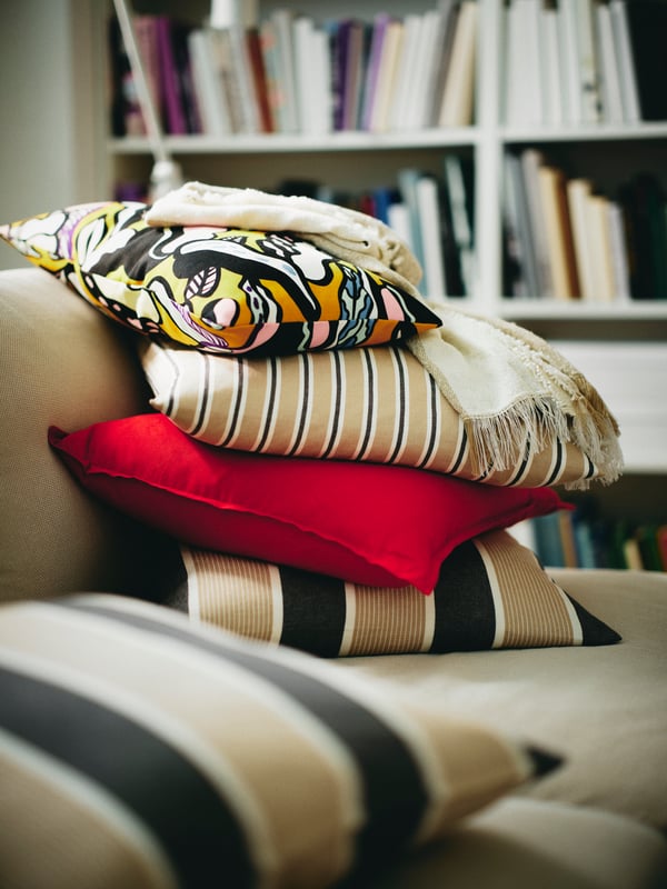 A pile of cushions dressed in GURLI and KORALLBUSKE cushion covers and a multicolour/leaf pattern SANDMOTT cushion.