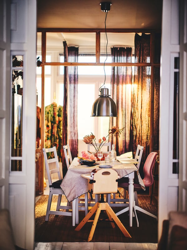 A GRÅVAL junior highchair with tray, placed in a dining room, near an extendable table, chairs, a pendant lamp and curtains.