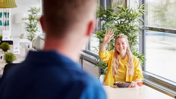 Smiling IKEA co-worker inviting a colleague to join her for lunch in the canteen.