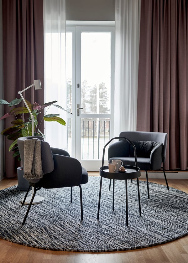 Mysig vardagsrumshörna med två svarta BINGSTA fåtöljer på en rund, texturerad matta med ett litet runt bord framför ett stort fönstr.