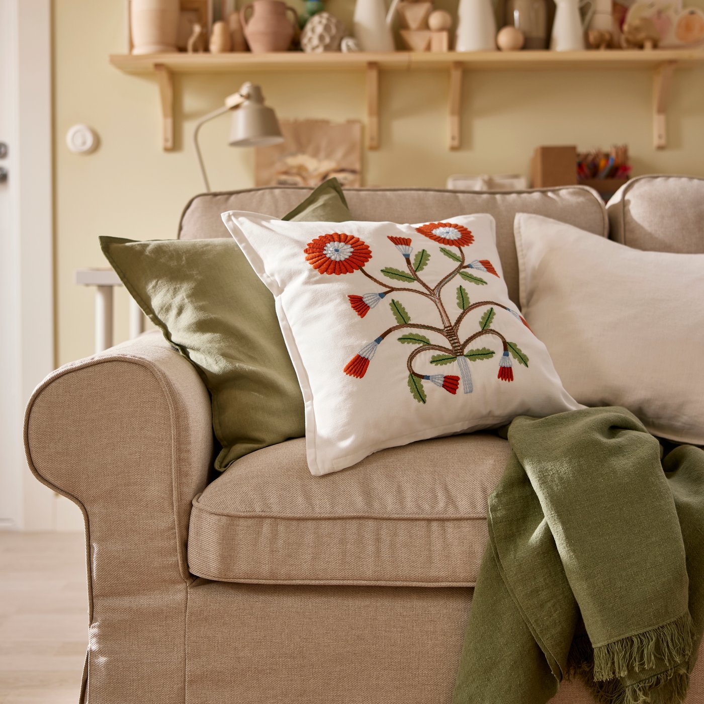 Närbild på en vit kudde med en röd blomma liggande i beige soffa.