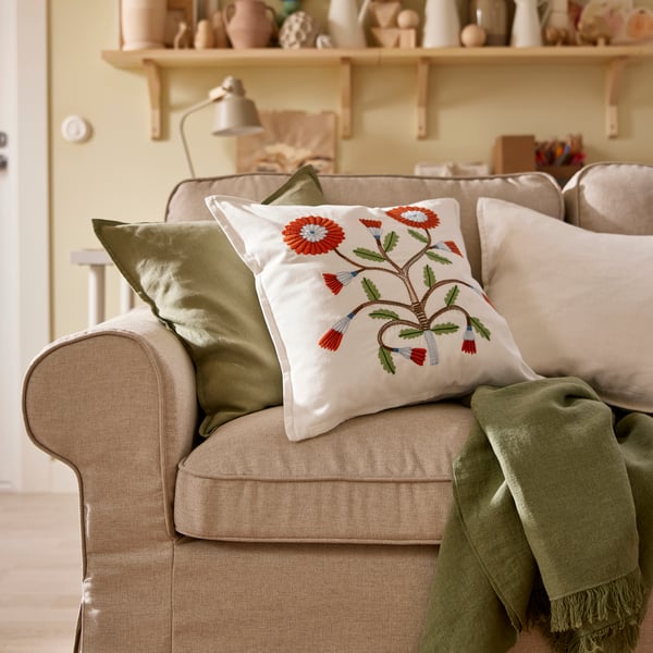 A DYTÅG throw and three cushions, including one with a flowery FACELIOR cushion cover, lie on an EKTORP sofa.