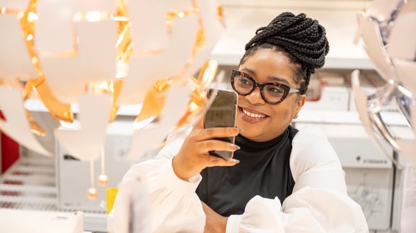 Femme assise sur une chaise et tenant une télécommande TRÅDFRI pour contrôler une ampoule LED connectée de IKEA.