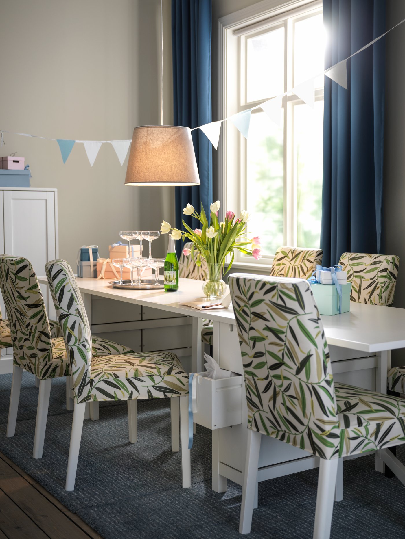 Sillas de comedor BERGMUND color blanco con funda con diseño de hojas multicolor, frente a una mesa abatible blanca.