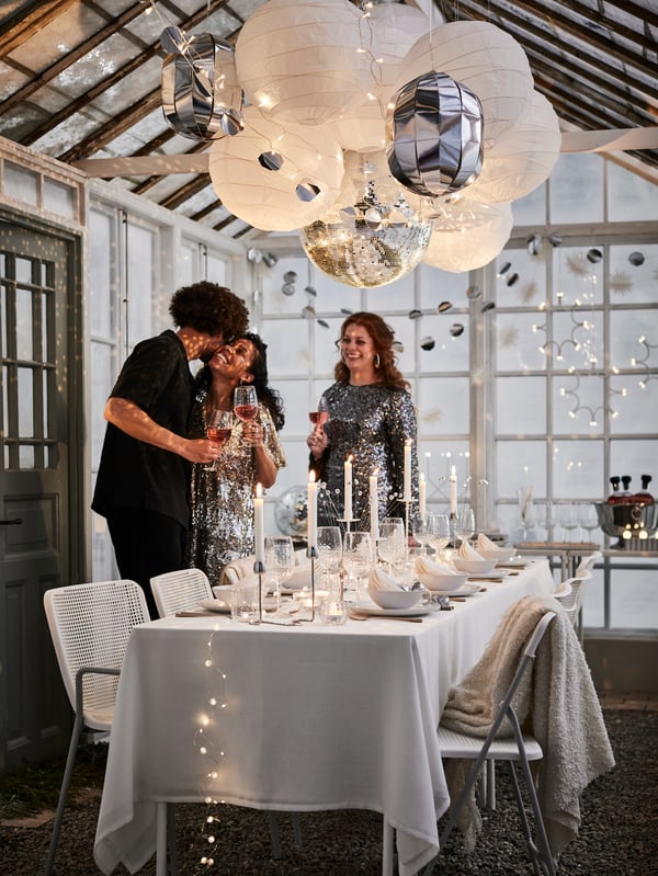 White and silver themed New Year’s Eve dining setting in greenhouse with FRÖJDA hanging decoration, garlands and lighting.