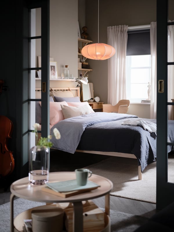 Parted glass doors open onto a bedroom with a BJÖRKSNÄS birch bed, dark-blue KOPPARBLAD bed linen, and a desk and chair.