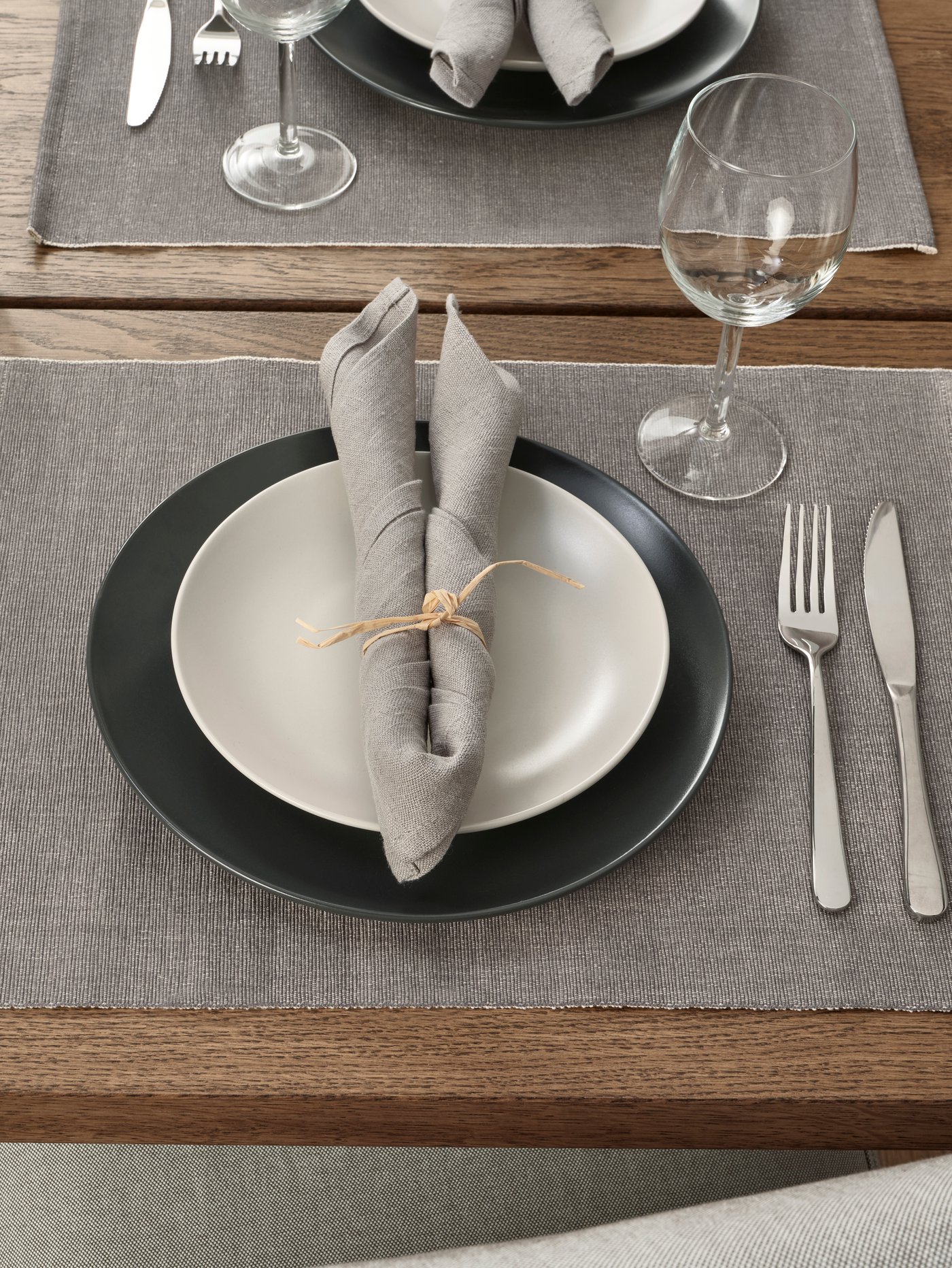 Individual IKEA de color gris con platos , cubiertos y una copa encima.