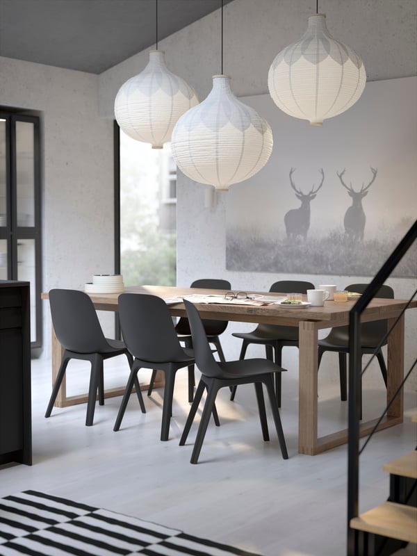 A room with a MÖRBYLÅNGA table in oak veneer brown stained, with ODGER chairs in anthracite and RISBYN pendant lampshades.