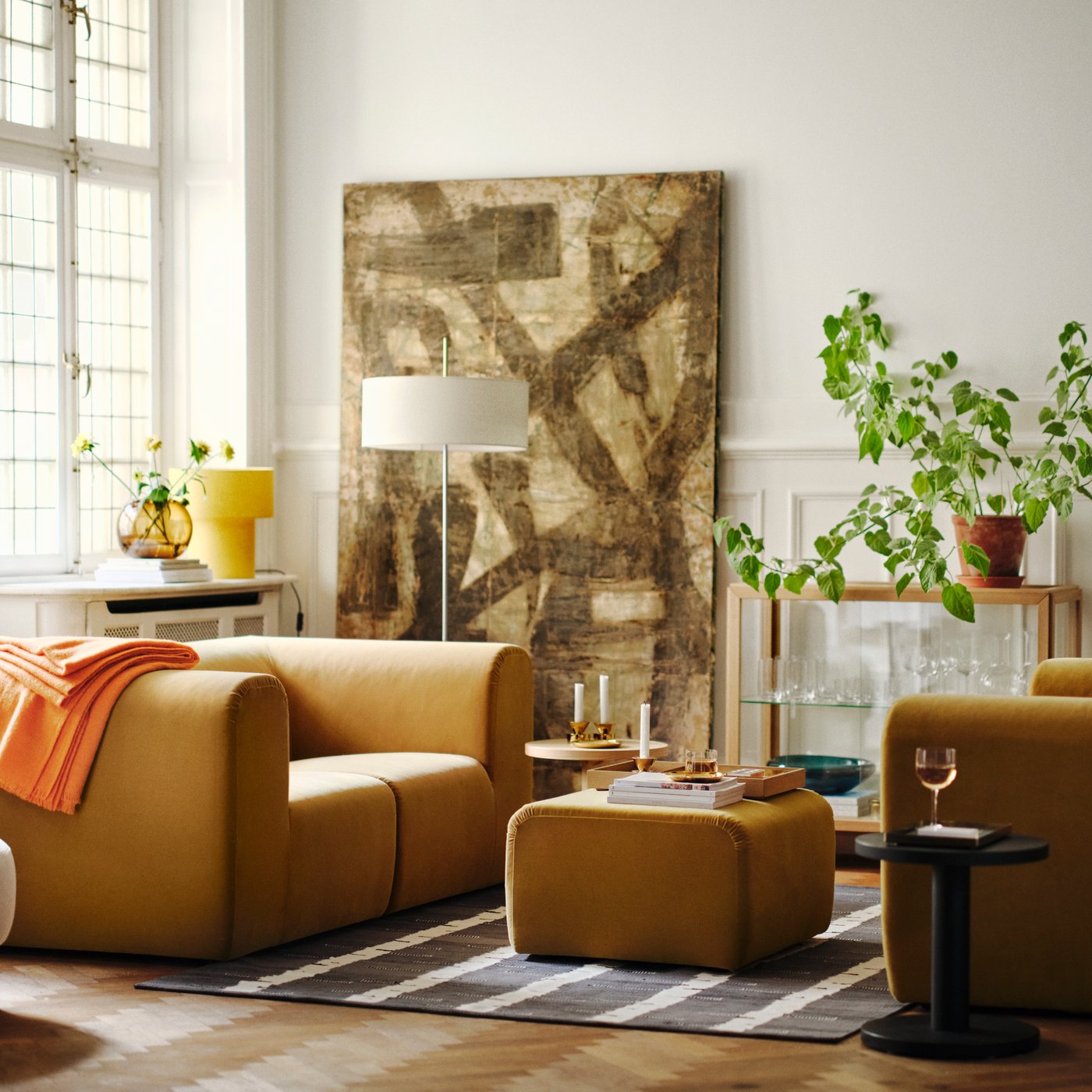 A bright living room with two beige STOCKHOLM 2025 2-seat sofas facing each other, with a pouffe on a rug between them.