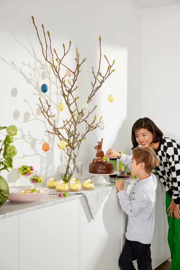 A woman and a child looking at a counter with a VÅRKÄNSLA milk chocolate bunny and some VÅRKÄNSLA milk chocolate eggs on it.
