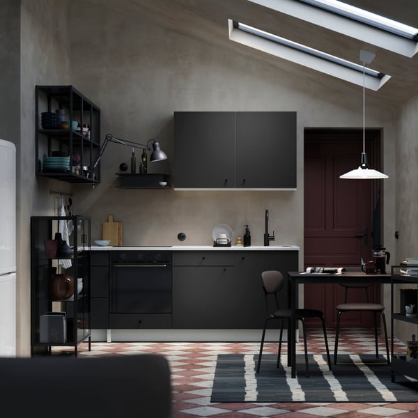 A stylish and monochromatic space with a KNOXHULT kitchen in dark grey, a slanted ceiling and a dining area.