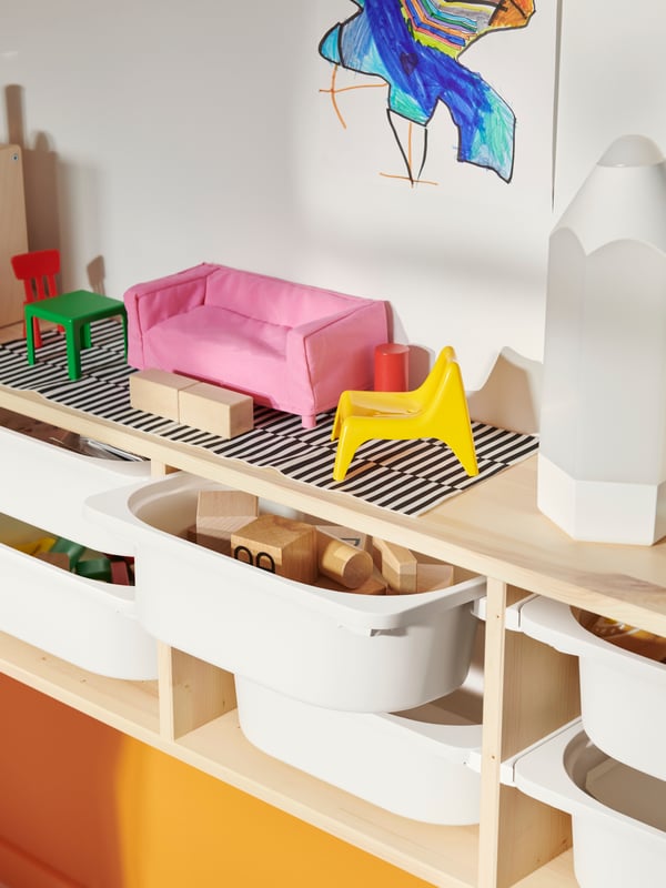 Various colourful toys on top a light white stained pine TROFAST wall storage filled with white storage boxes.