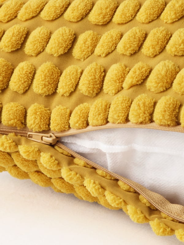 A close-up of an open zip on a yellow SVARTPOPPEL cusion cover revealing the cushion inside.