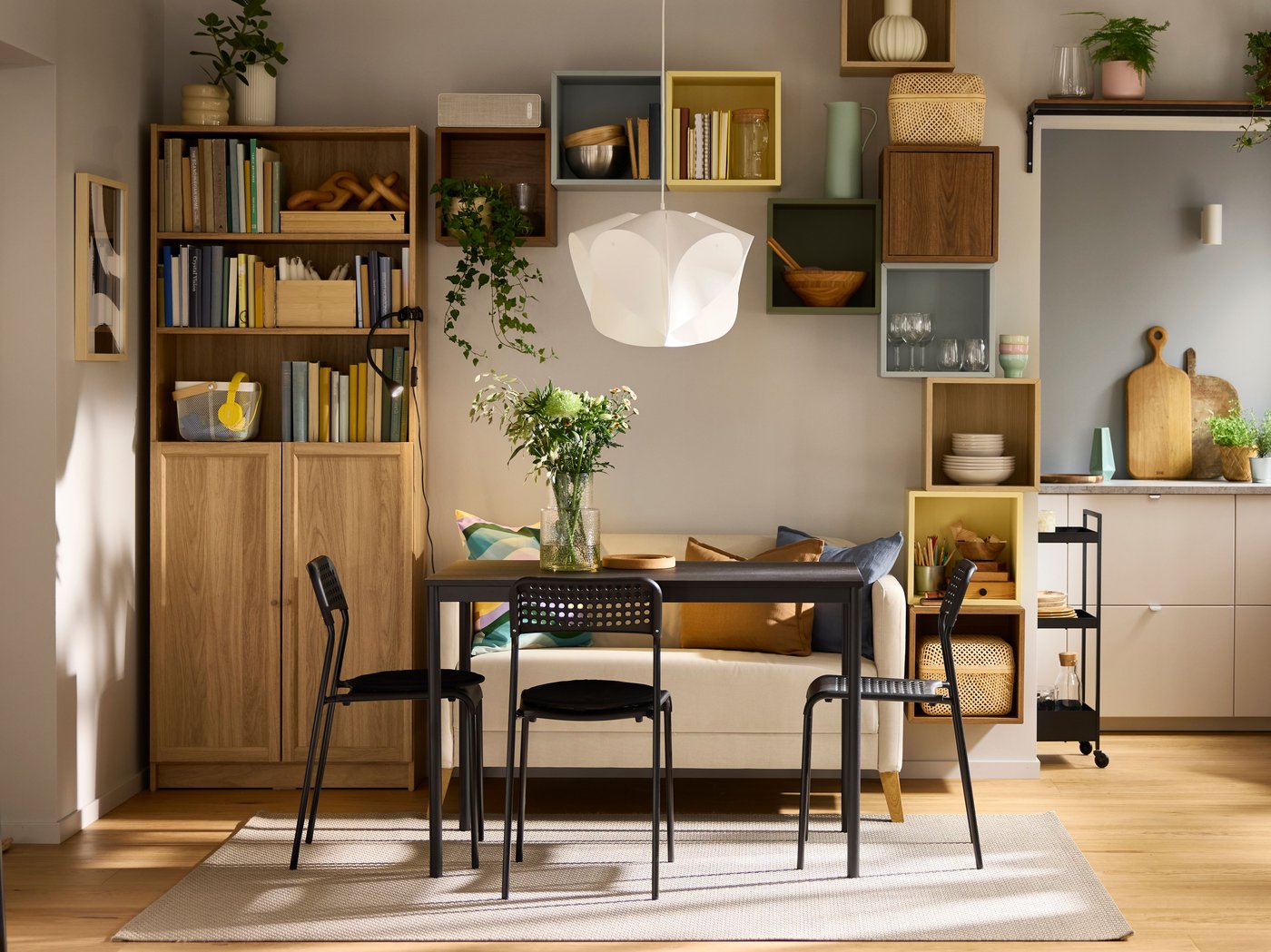 A bright dining room with wood and pastel notes where a black SANDSBERG table is framed by ADDE chairs and a LINANÄS sofa.